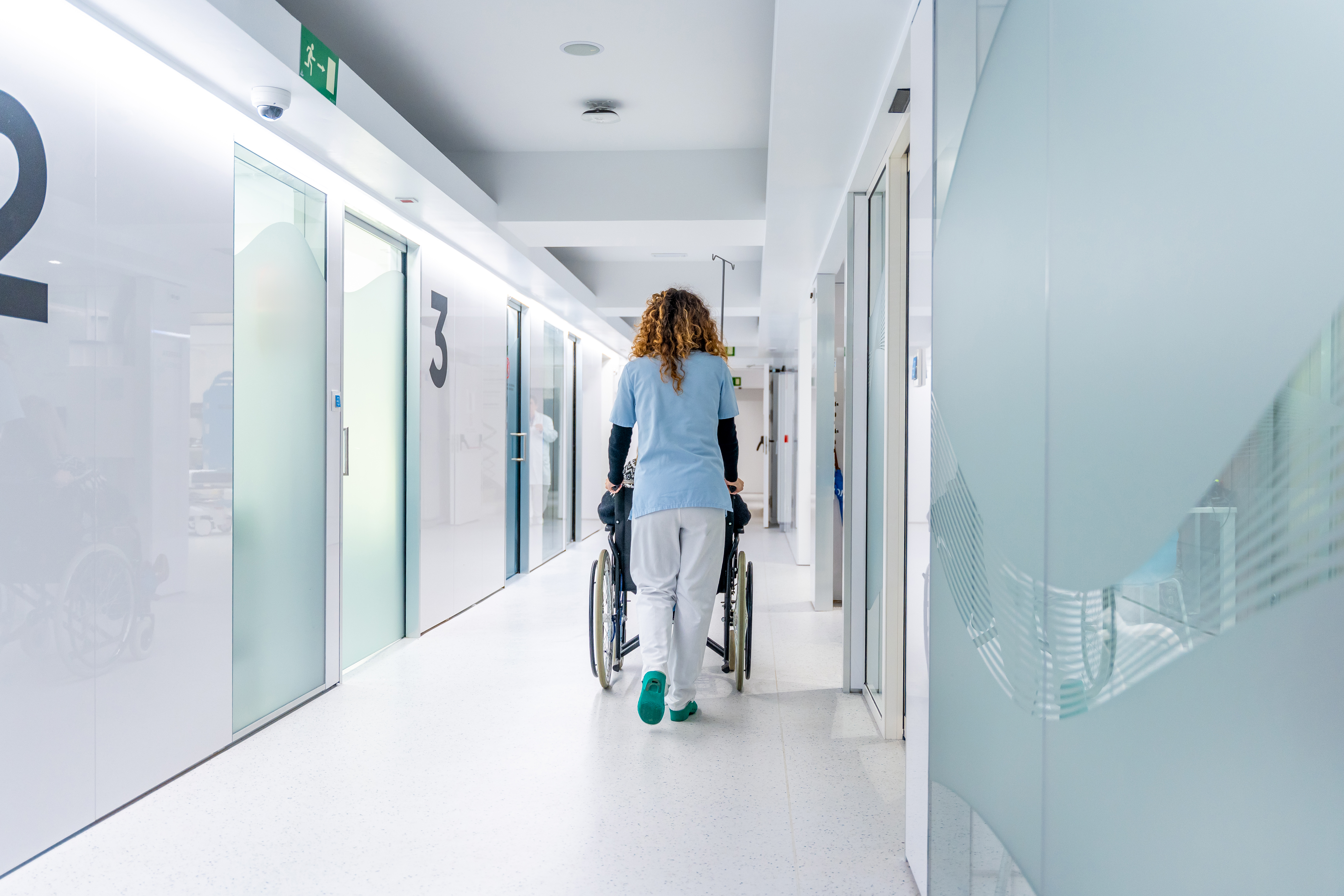 Vista posterior de la infermera empenyent una cadira de rodes per l'hospital